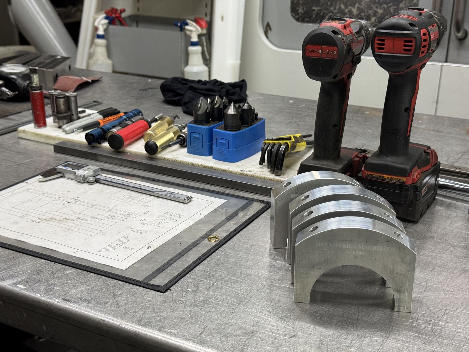 Inspection tools, edge finders, calipers, and a print laid out next to a finished semicircular aluminum part